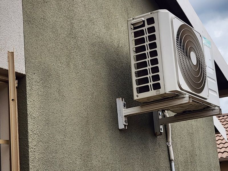 Exterior view of a residential property featuring a wall-mounted air conditioning condenser unit and tiled roof section.