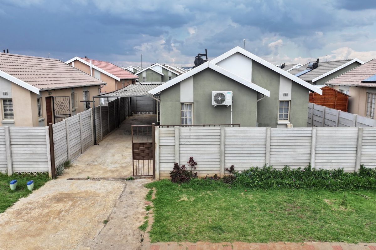 Rear view of a detached house featuring a private driveway, carport, precast concrete boundary wall, and an installed air conditioning unit.