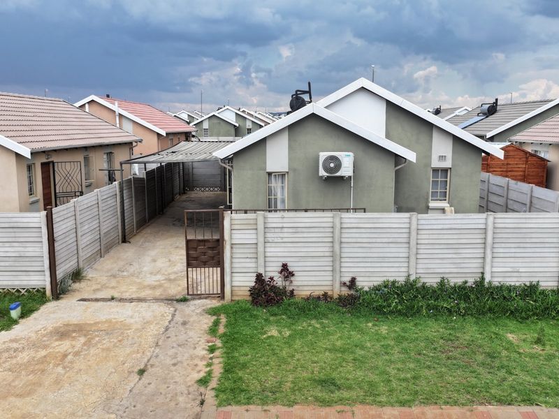 Rear view of a detached house featuring a private driveway, carport, precast concrete boundary wall, and an installed air conditioning unit.