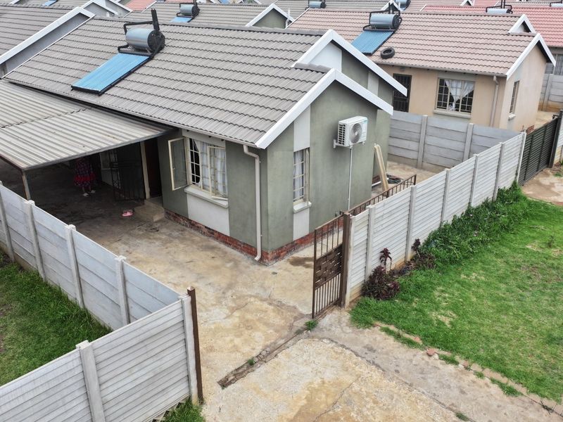 Aerial view of a detached residential house featuring a tiled roof, solar water heating system, carport, and enclosed garden with precast boundary walls.