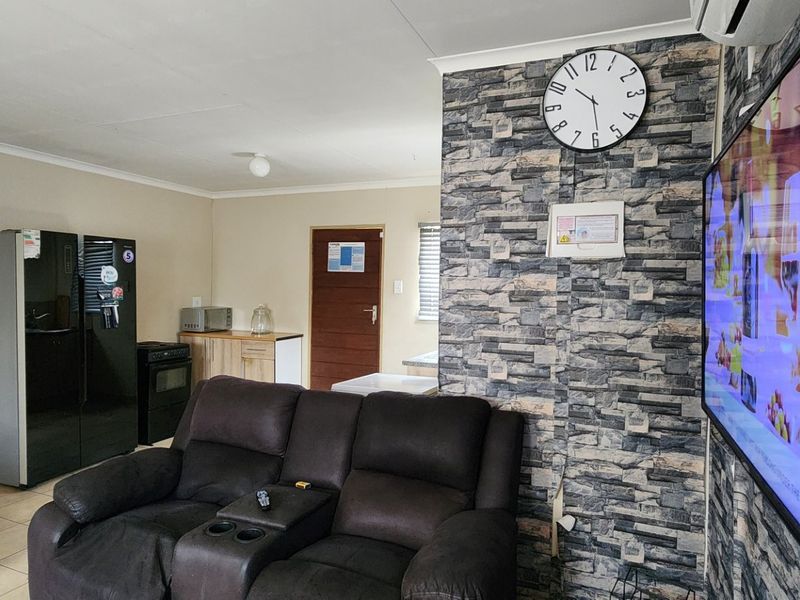 Open-plan living area featuring a stone-cladding accent wall, tiled flooring, and an integrated kitchen space with built-in cabinetry.