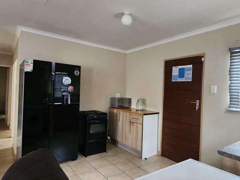 A functional kitchen area featuring tiled flooring, built-in cabinetry, a stainless steel sink, and venetian blinds, providing a practical layout for daily use.