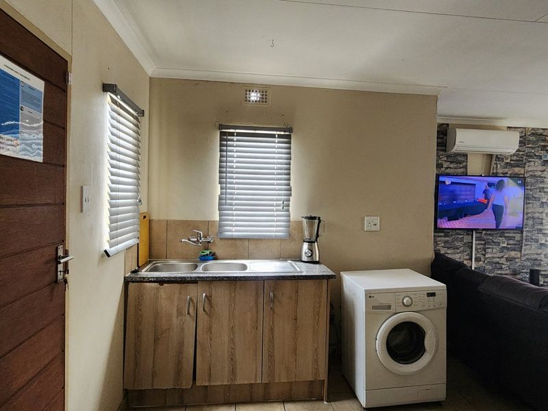 Open-plan living area featuring a compact kitchenette with laminate cabinetry, tiled flooring, and a split-system air conditioner.