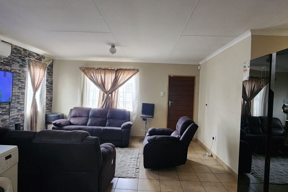 A living room featuring tiled flooring, a stone-effect feature wall, and an integrated air conditioning unit.