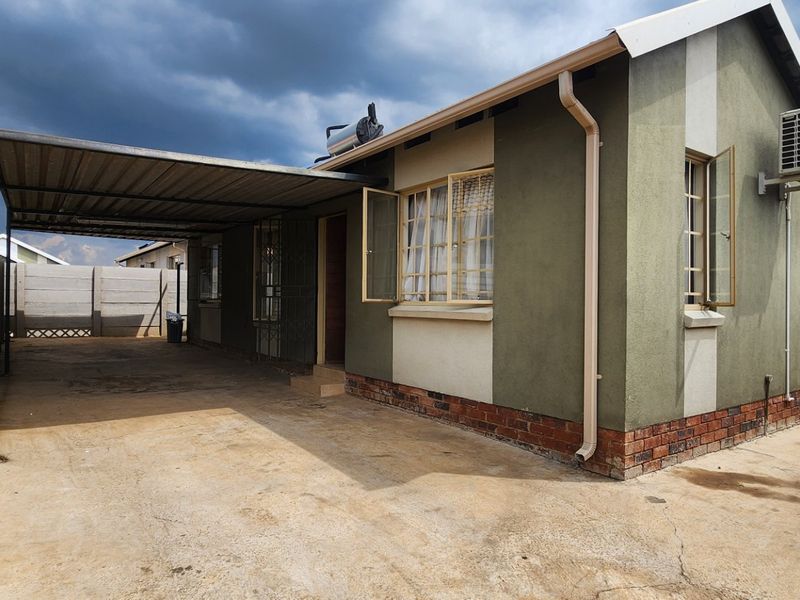 Rear exterior view of the house featuring a covered carport, solar water heating system, and wall-mounted air conditioning unit within a fenced yard.