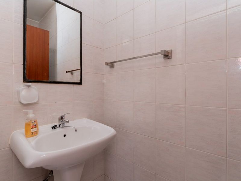 A compact bathroom featuring a white pedestal washbasin, chrome fixtures, and neutral ceramic wall tiling.