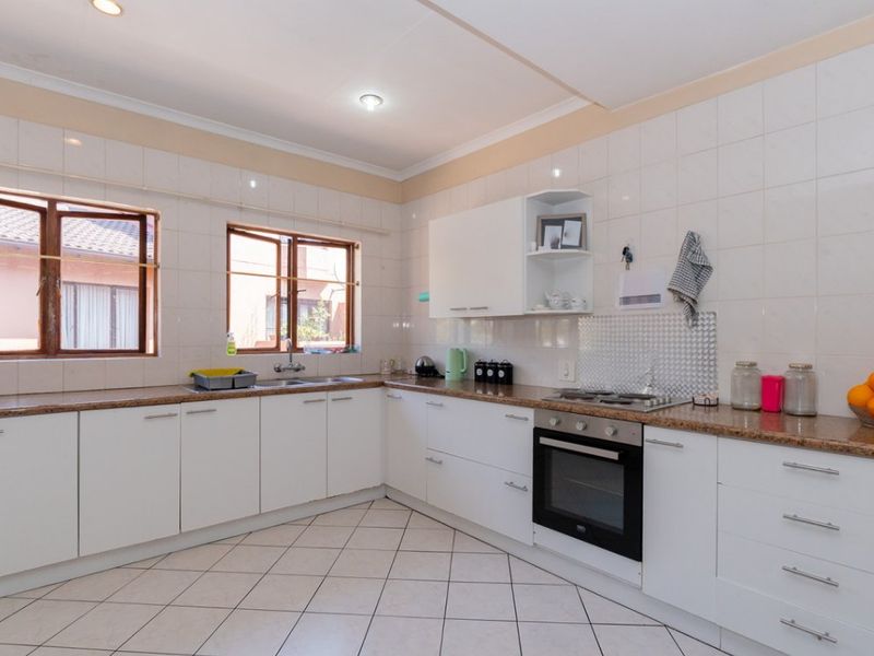 A functional kitchen featuring white cabinetry, granite countertops, a built-in oven, gas hob, and tiled flooring with ample natural light.