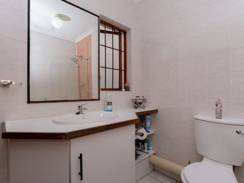 A functional bathroom featuring a vanity cabinet with integrated sink, wall-mounted mirror, toilet, and a shower area with tiled finishes.