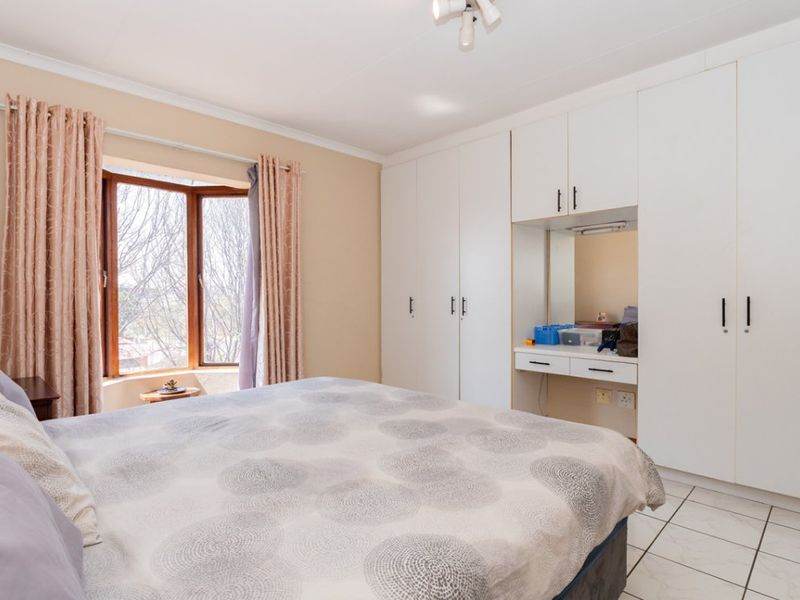 A bedroom featuring built-in cupboards with an integrated vanity area, tiled flooring, and a bay window providing natural light.