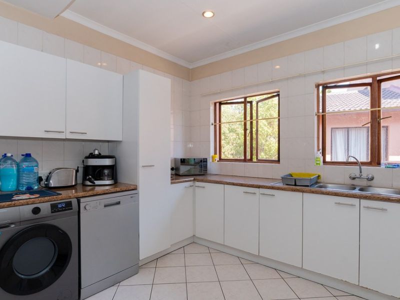A functional kitchen featuring white cabinetry, laminate countertops, tiled backsplash, and tiled flooring with ample natural light from two windows.