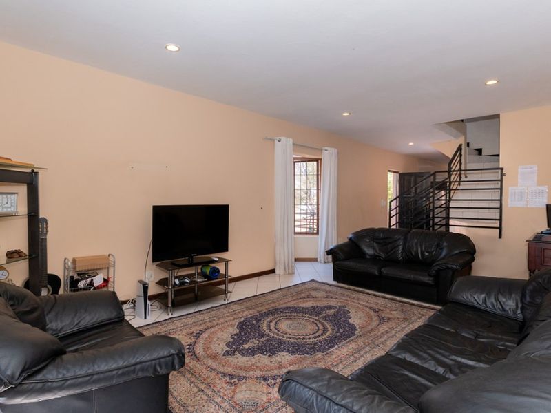 Spacious living room featuring tiled flooring, recessed lighting, and an internal staircase with a metal balustrade.