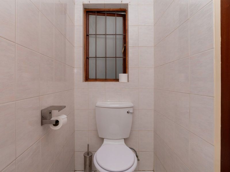 A compact, fully tiled bathroom featuring a standard toilet and a small window with security bars.