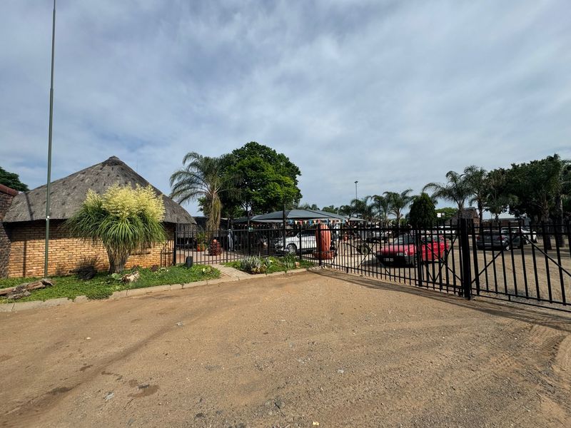 Front entrance view of the commercial property featuring a gravel driveway, metal security gate, and a traditional thatch-roofed building.