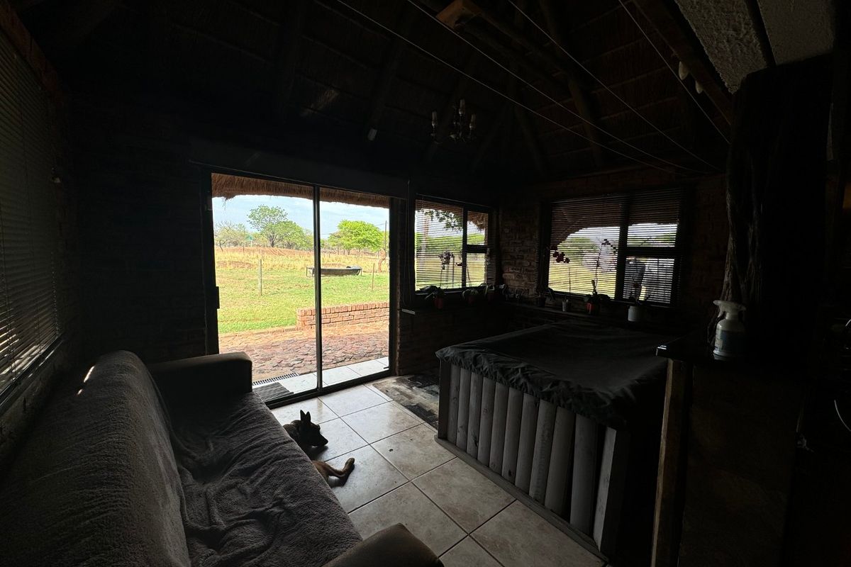 A rustic living area featuring exposed brick walls, a traditional thatched roof with timber rafters, tiled flooring, and sliding glass doors leading outdoors.