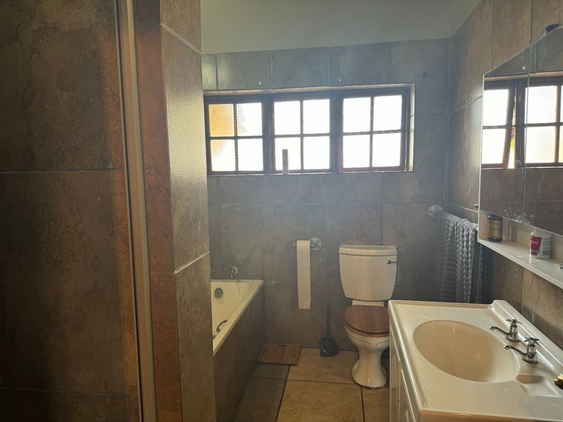 A functional bathroom featuring a built-in bathtub, toilet, and vanity basin with full-height wall tiling and a window for natural light.