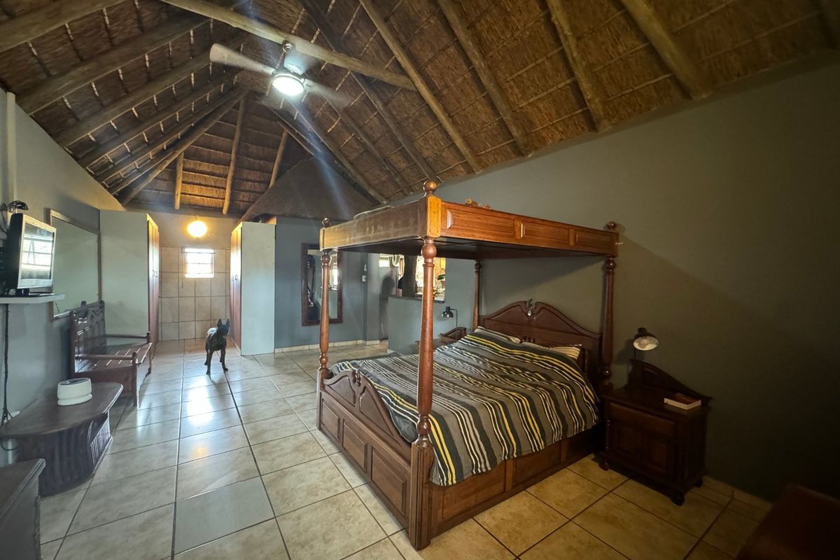 Spacious bedroom featuring a high vaulted thatched roof with exposed timber rafters, ceramic tiled flooring, and built-in storage cabinetry.