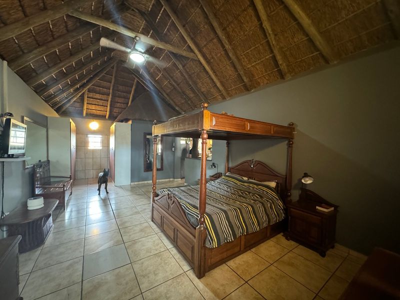 Spacious bedroom featuring a high vaulted thatched roof with exposed timber rafters, ceramic tiled flooring, and built-in storage cabinetry.