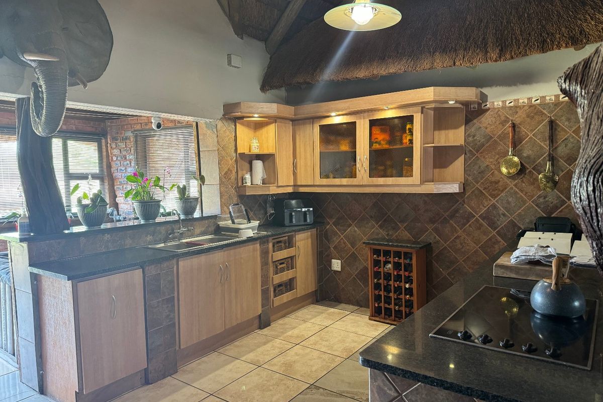 A rustic kitchen featuring wooden cabinetry, granite countertops, tiled backsplash, and a distinctive thatched roof ceiling, offering a warm and traditional aesthetic.