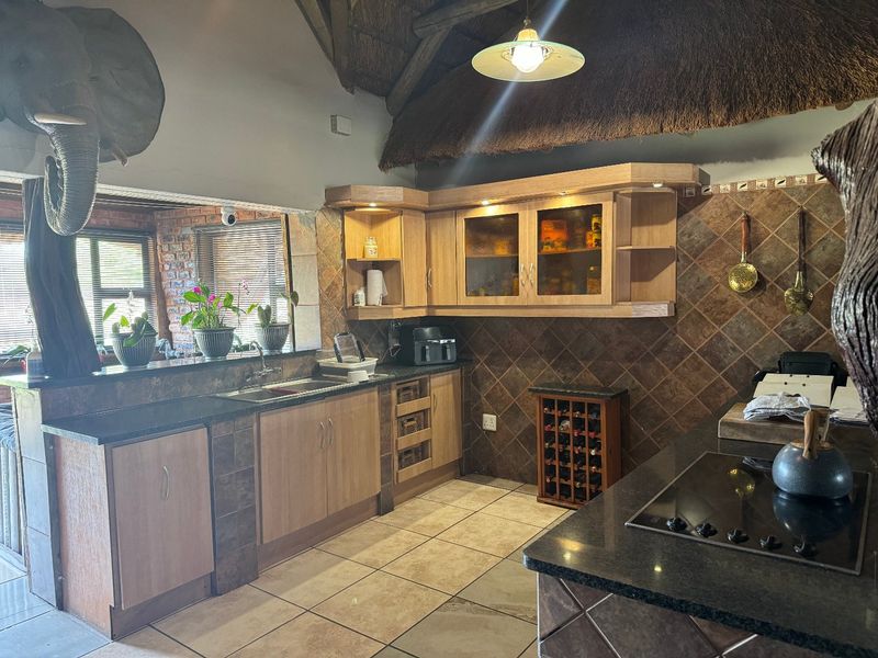 A rustic kitchen featuring wooden cabinetry, granite countertops, tiled backsplash, and a distinctive thatched roof ceiling, offering a warm and traditional aesthetic.