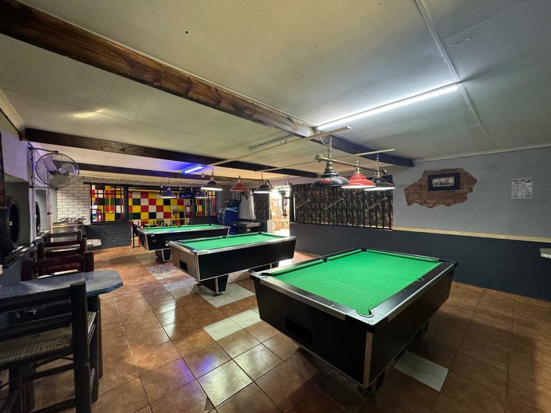 A commercial sports facility featuring tiled flooring, exposed timber ceiling beams, and multiple pool tables with dedicated overhead lighting.