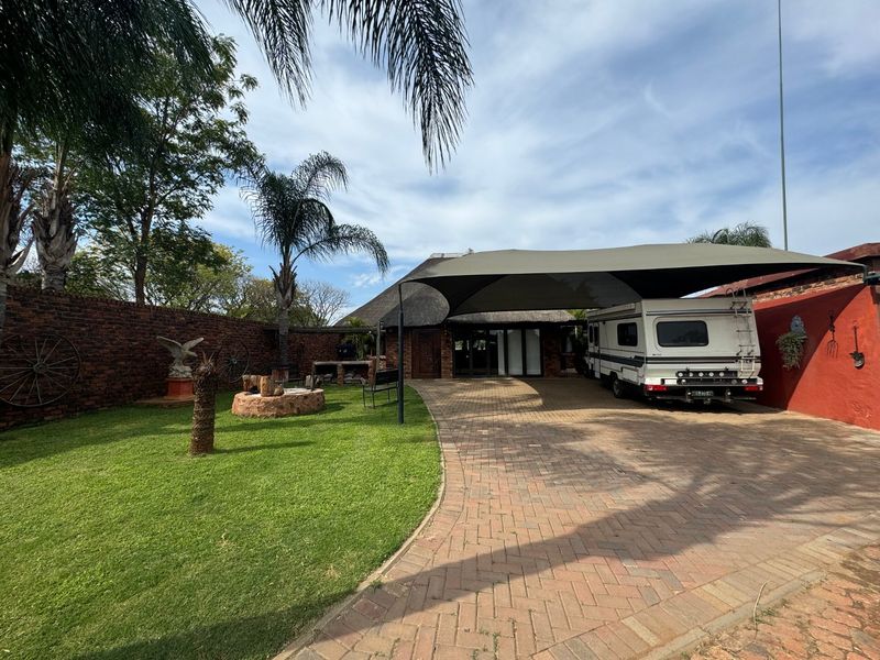 Rear exterior area featuring brick paving, a shade sail carport, a built-in braai, and a landscaped garden with a brick boundary wall.