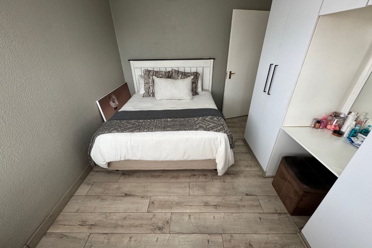 A well-maintained bedroom featuring wood-look tile flooring and built-in white cabinetry with an integrated vanity desk.