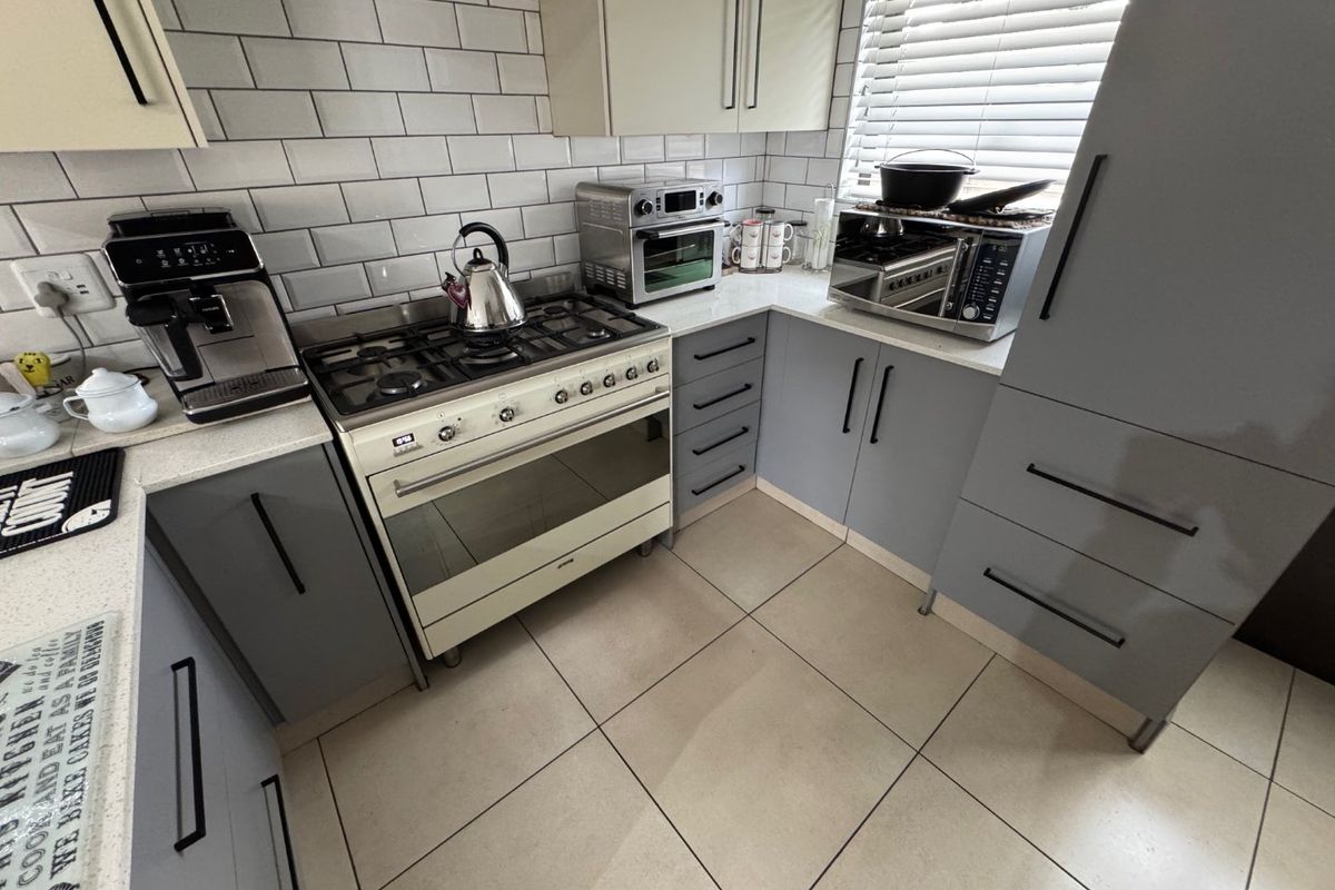 Modern kitchen featuring grey cabinetry, white subway tile backsplash, stone countertops, and a freestanding gas stove with an integrated extractor fan.