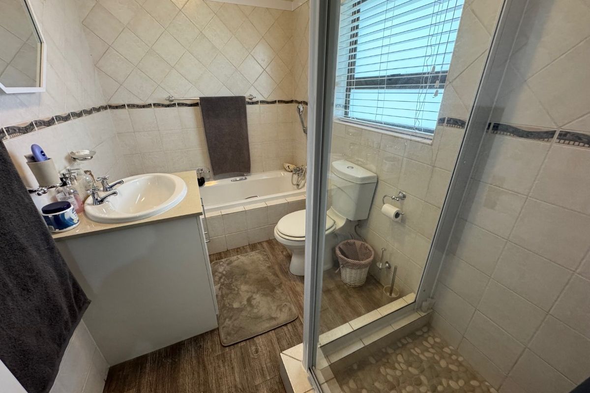 A functional bathroom featuring a built-in vanity, a bathtub with shower attachment, and a separate glass-enclosed shower stall with pebble-style flooring.
