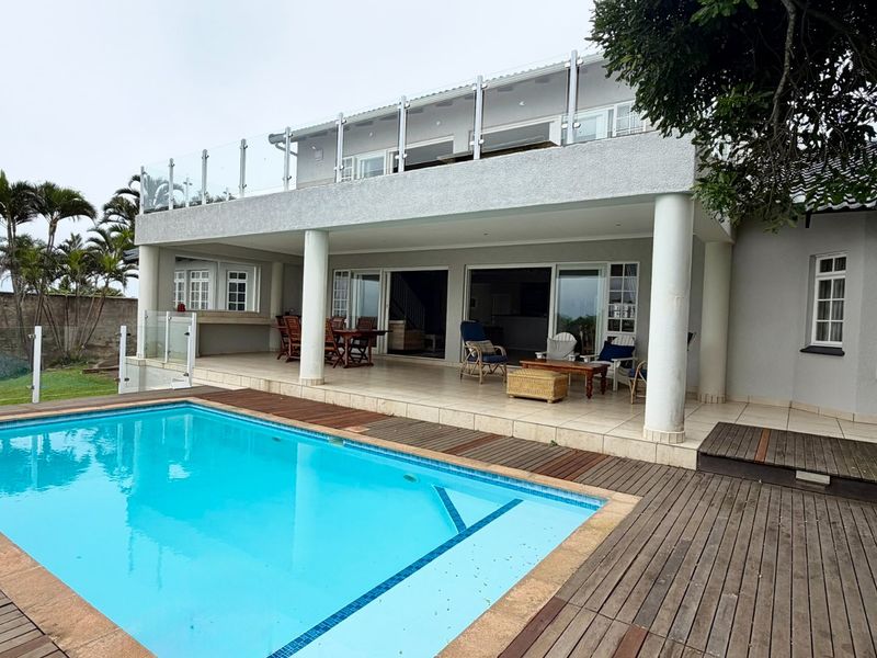 Spacious outdoor entertainment area featuring a swimming pool, timber decking, and a covered patio with glass balustrades overlooking the garden.