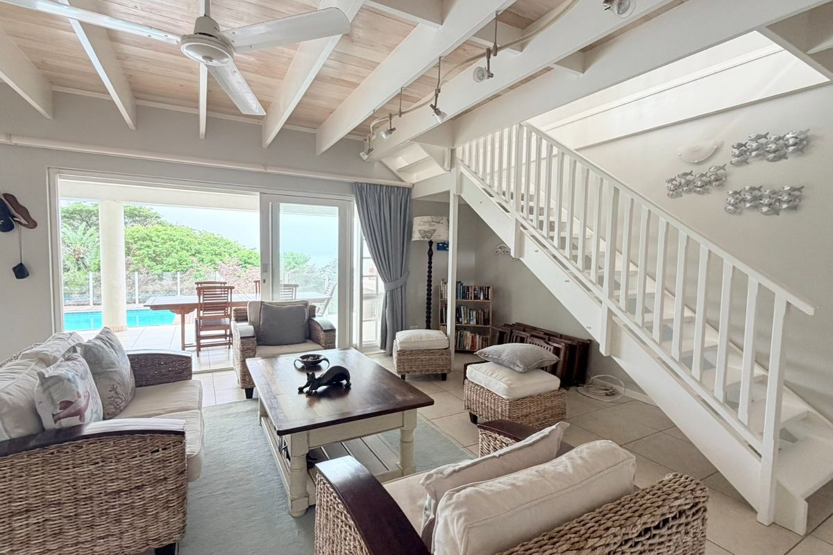 Spacious living area featuring exposed beam ceilings, a staircase, and large sliding glass doors providing seamless access to the outdoor patio and pool area.