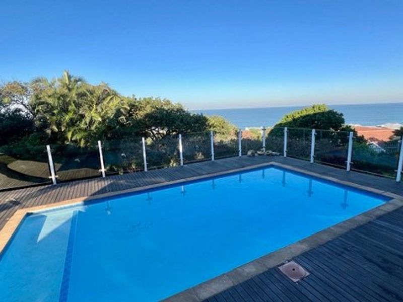 A well-maintained swimming pool area featuring timber decking and a modern glass balustrade, offering scenic ocean views.
