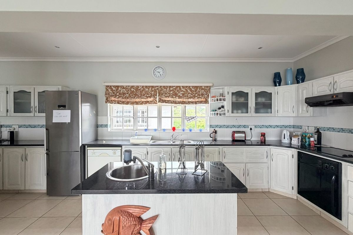 A spacious kitchen featuring white cabinetry, granite countertops, a central island with a prep sink, and tiled flooring throughout.
