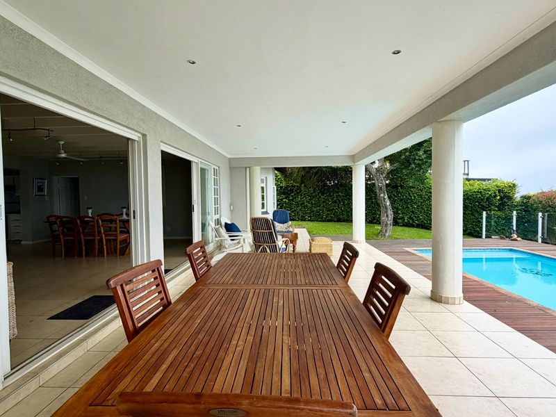Spacious covered patio featuring tiled flooring and recessed lighting, seamlessly connecting to the interior living area and overlooking the swimming pool and garden.