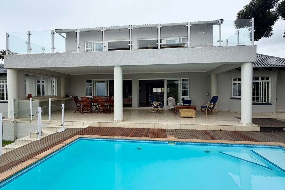 Spacious rear exterior featuring a tiled patio, swimming pool with wooden decking, and a large upper-level balcony with glass balustrades.