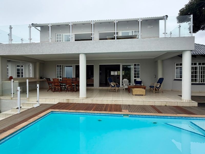 Spacious rear exterior featuring a tiled patio, swimming pool with wooden decking, and a large upper-level balcony with glass balustrades.