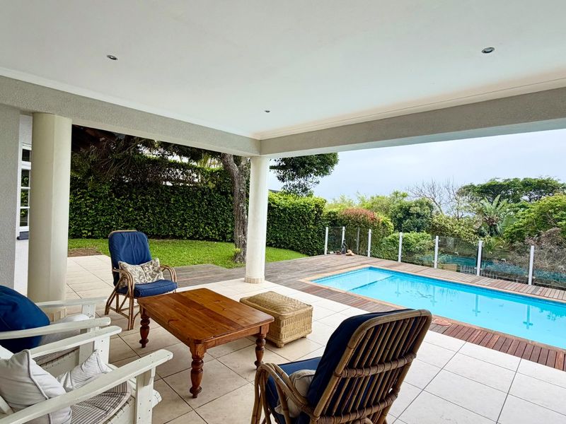 A spacious covered patio featuring tiled flooring and recessed lighting, overlooking a private swimming pool with timber decking and a glass balustrade.