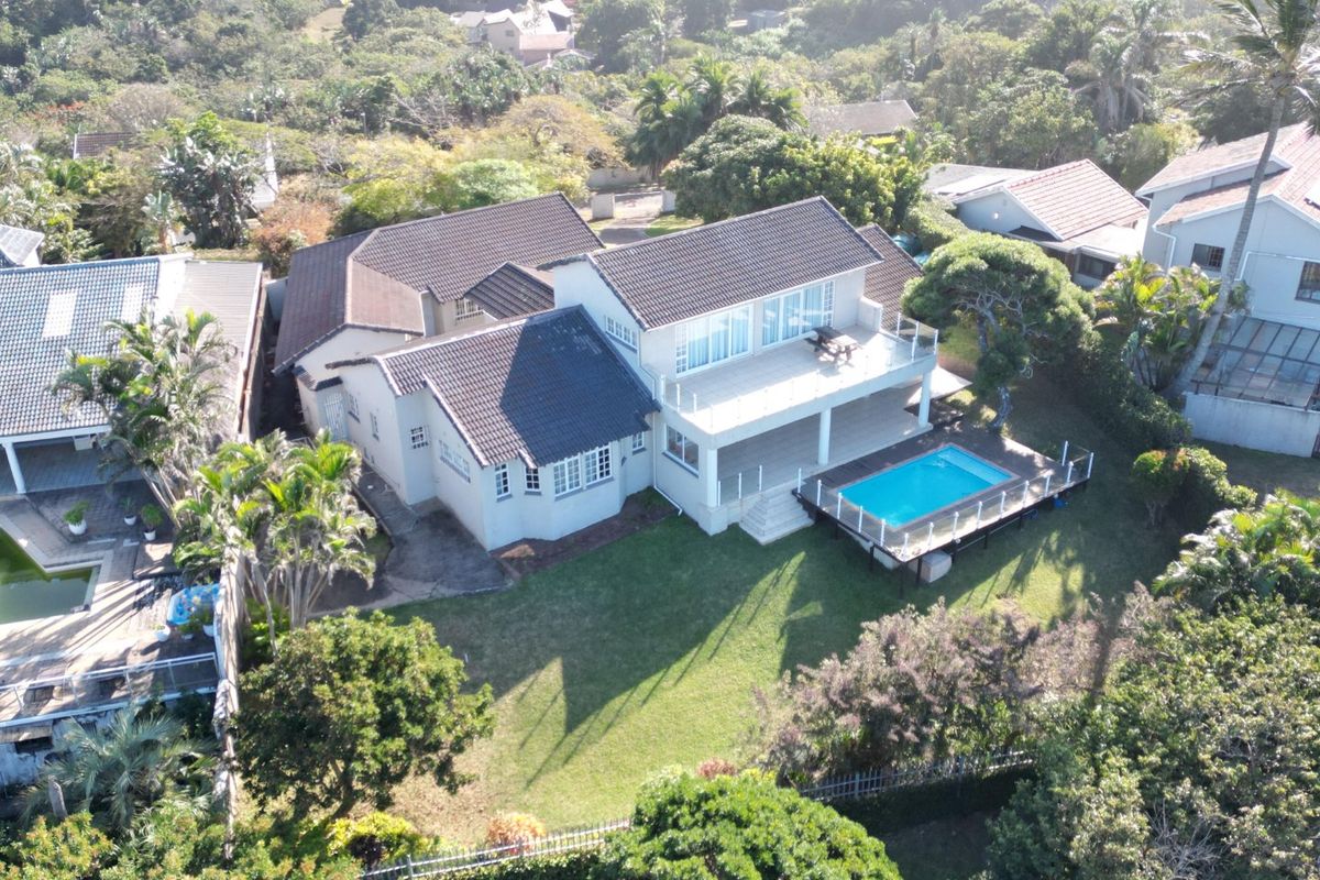 Aerial view of a residential property featuring a tiled roof, a swimming pool with a wooden deck, and an elevated balcony.