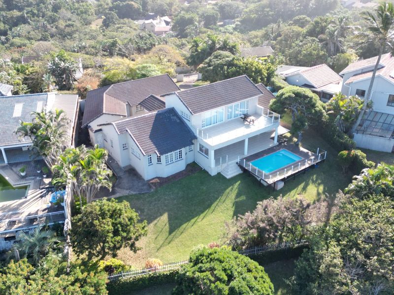 Aerial view of a residential property featuring a tiled roof, a swimming pool with a wooden deck, and an elevated balcony.
