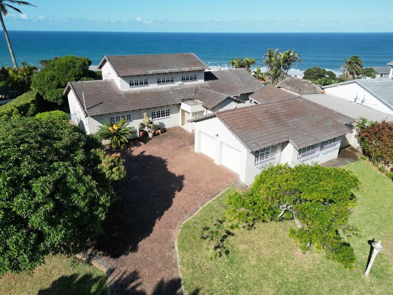 Aerial view of a coastal property featuring a tiled roof, double garage, paved driveway, and expansive ocean views.