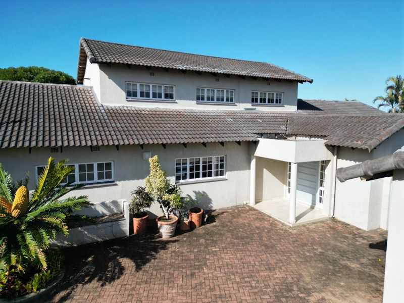 An elevated view of the front facade featuring a tiled roof, paved driveway, and a covered entrance porch.