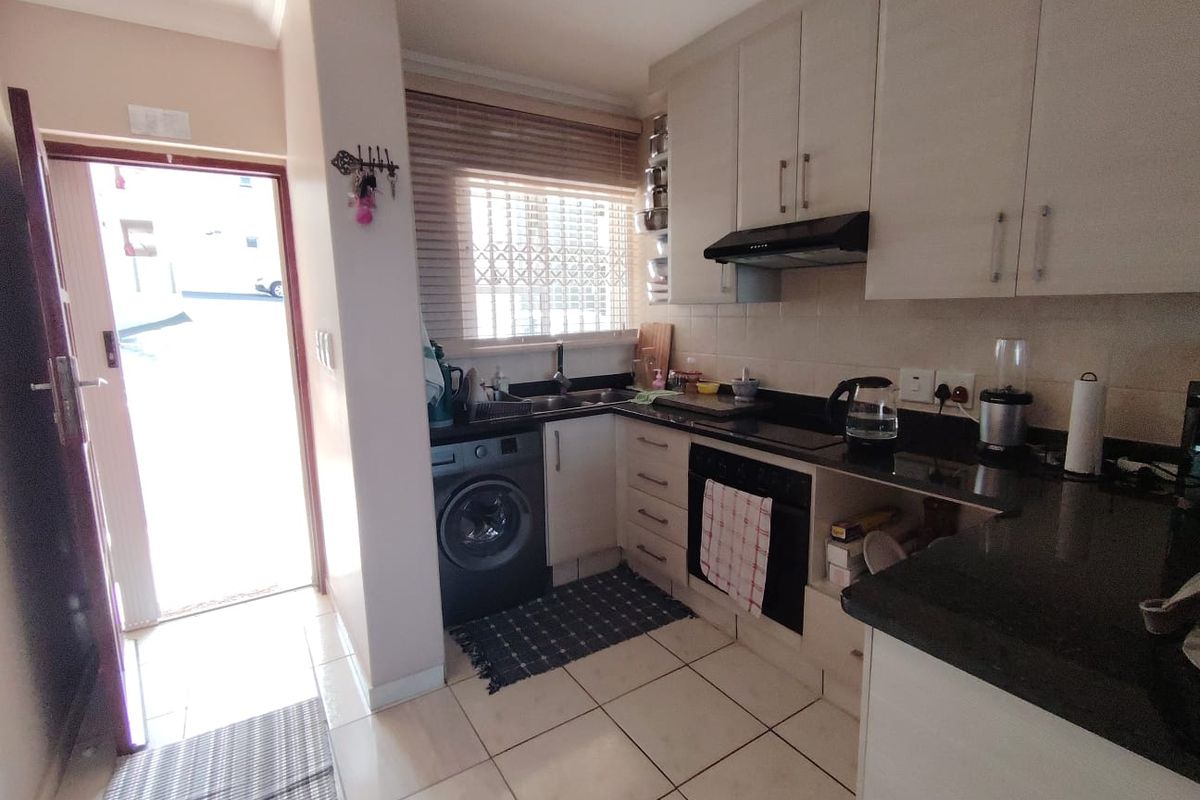 Compact kitchen featuring built-in cabinetry, granite countertops, integrated oven, extractor fan, and tiled flooring with direct access to the exterior.