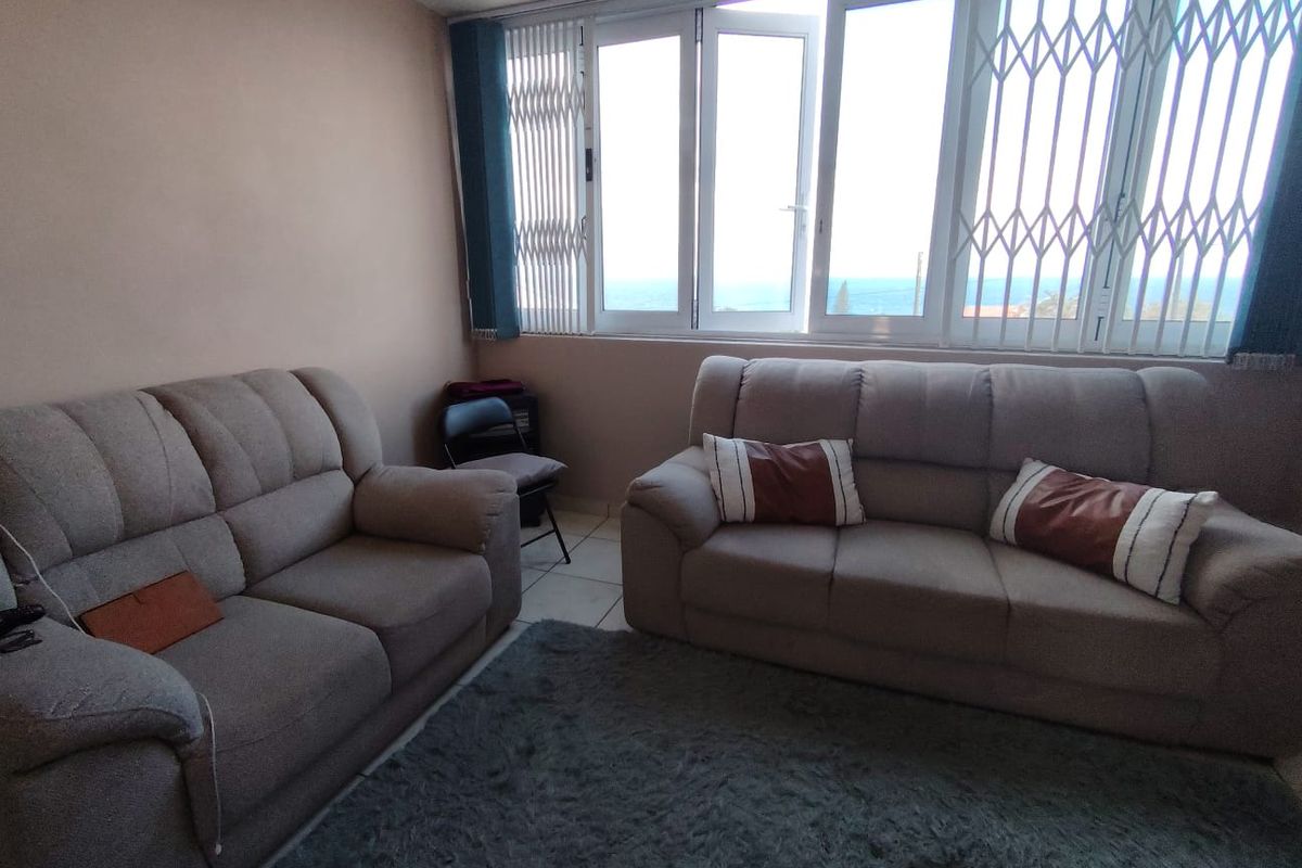 A living room area featuring tiled flooring and large windows with security gates, offering a view of the ocean.