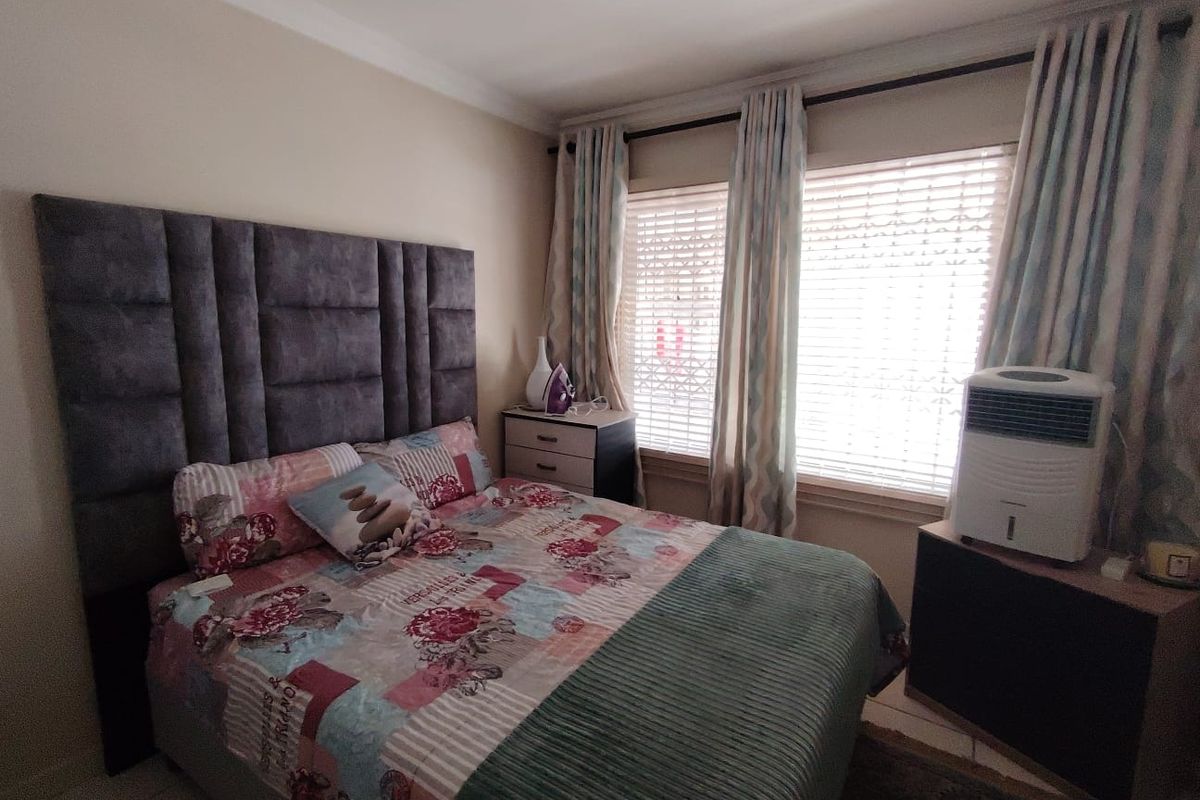A well-lit bedroom featuring neutral walls, coving, and window treatments including venetian blinds and curtain tracks.