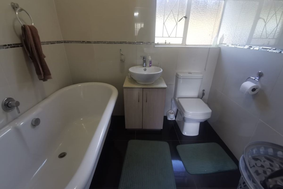 A functional bathroom featuring a freestanding bathtub, vessel sink with vanity cabinet, toilet, and tiled finishes throughout.