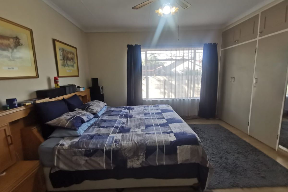 A functional bedroom featuring built-in cupboards, a ceiling fan, and security bars on the window, providing a comfortable and secure living space.