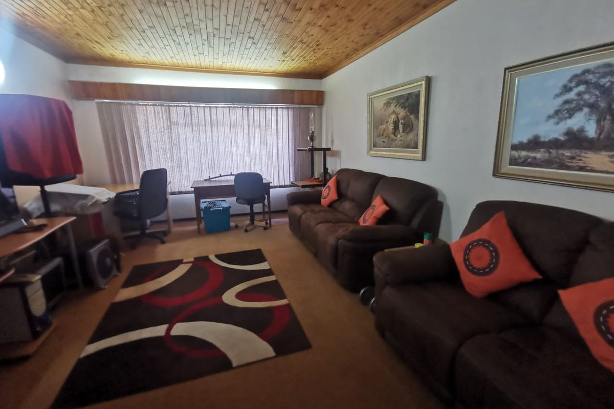 A living room featuring a timber tongue and groove ceiling and large window with vertical blinds.
