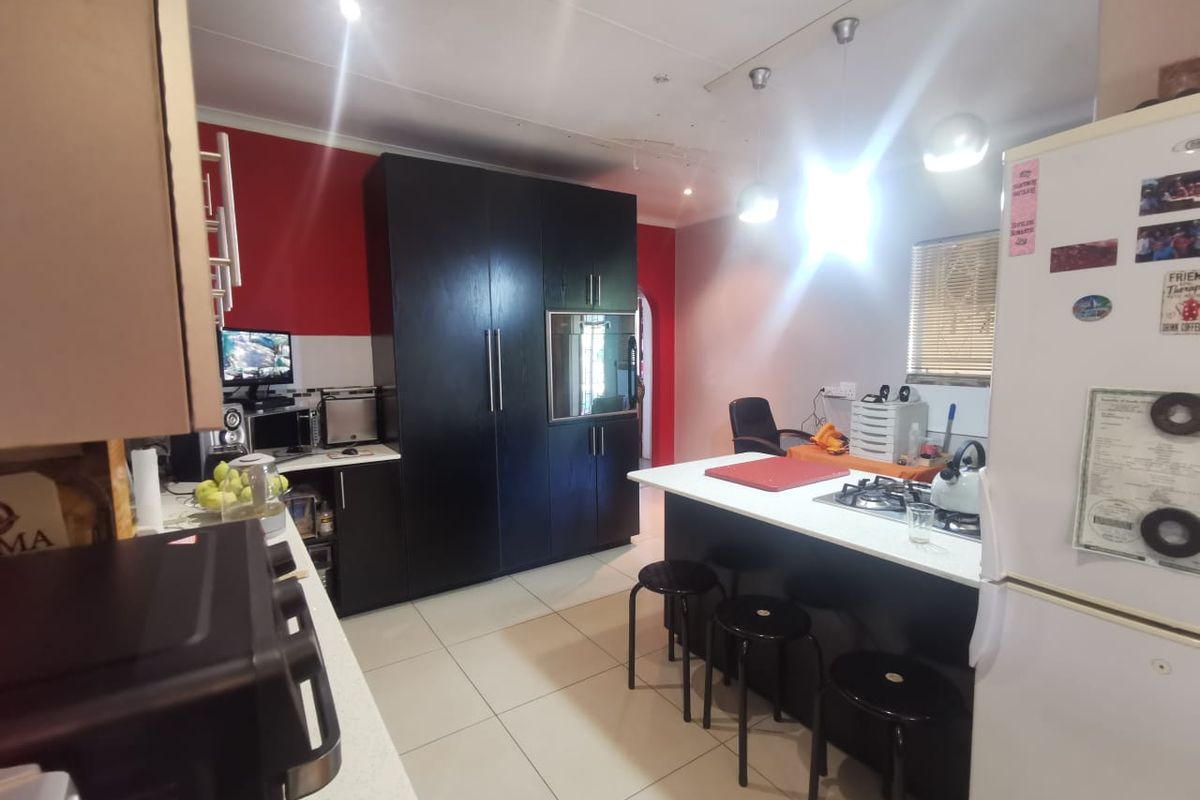 A functional kitchen featuring dark cabinetry, a central island with a gas hob, and tiled flooring, with visible ceiling damage requiring attention.