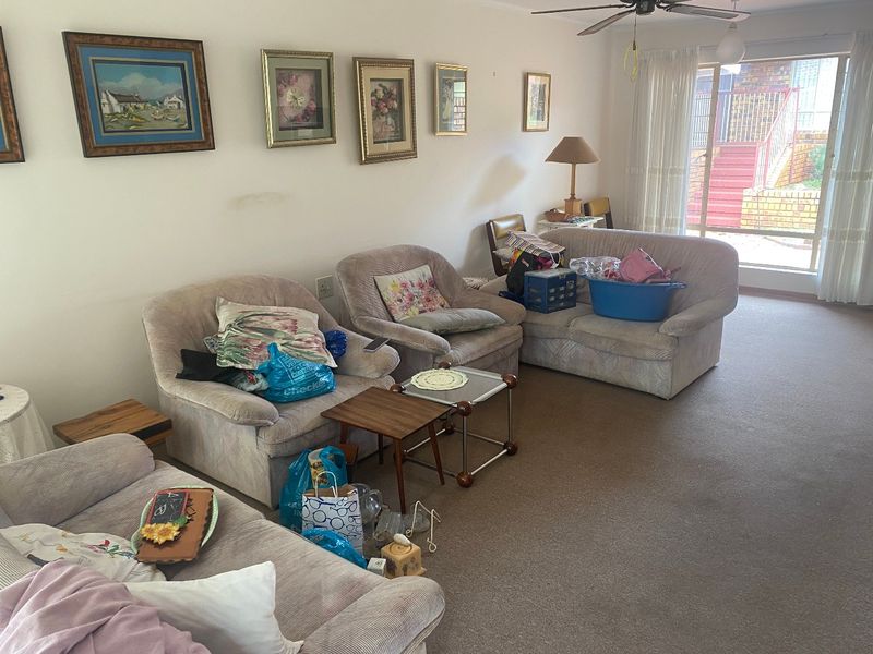 A spacious living room featuring neutral carpeting, a ceiling fan, and large sliding glass doors providing access to the exterior.