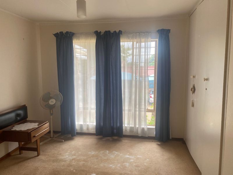 A bedroom featuring built-in cupboards and large windows with security bars. The room requires flooring updates to improve its overall condition.