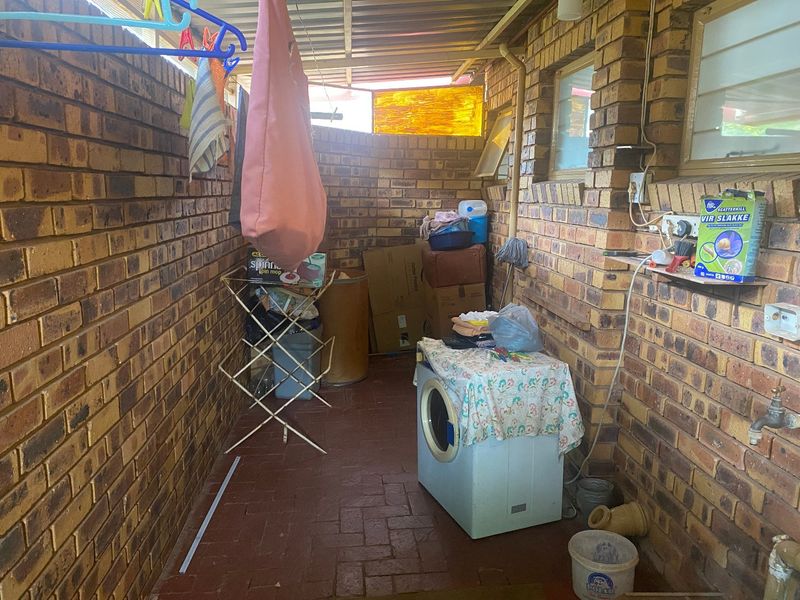 A functional outdoor laundry area featuring exposed brick walls, paved flooring, and essential plumbing connections for washing appliances.
